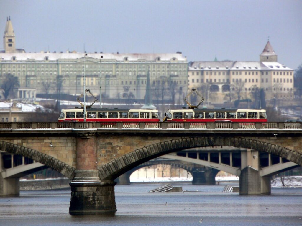 Red and cream Prague tram crossing a bridge with Prague Castle behind it